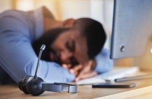 a man laying his head on a desk with headphones on and a laptop on the desk in front of him