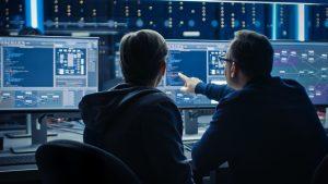 a couple of men sitting in front of a computer monitor in front of a monitor screen in a dark room