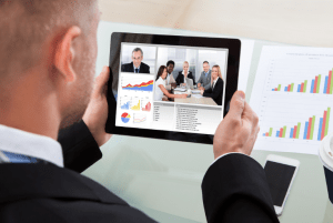 a man holding a tablet with a video of a business meeting on it and a cup of coffee in front of him