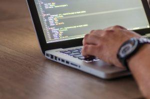 a close up of a developer working on a laptop on a wooden table with a hand on the keyboard